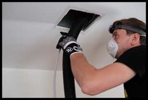 Duct cleaning in Ocean County being done by man wearing black t-shirt, black work gloves, face mask and a head lamp.